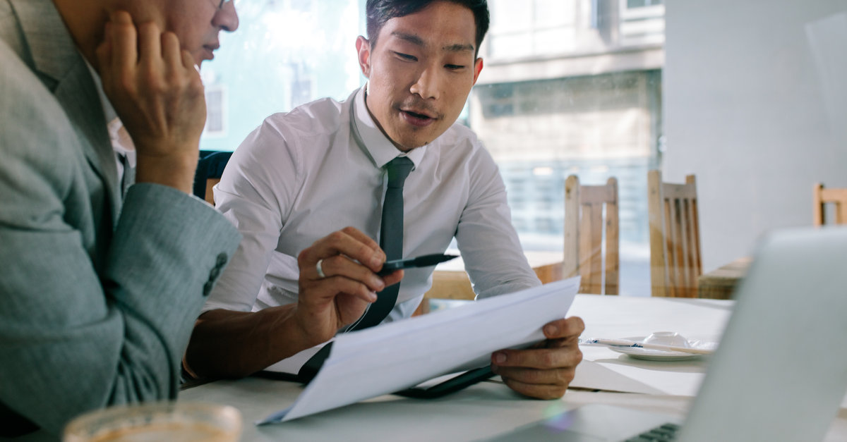 Young asian businessman explaining a document to his manager sitting at cafe table. Business professionals discussing over some paperwork at coffee shop.